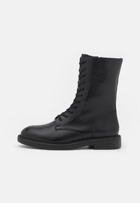 Bottines en cuir noir avec un bout arrondi, un laçage sur le devant, une texture lisse et une semelle plate en caoutchouc. Design simple, sans logos ni motifs visibles.