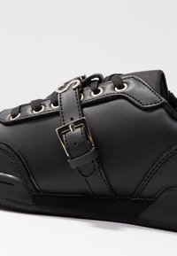 Baskets en cuir noir avec un design cintré, détail de boucle métallique, semelle texturée et lacets noirs passant par des œillets dorés.