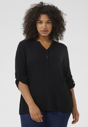 Chemise noire avec un col en V, des boutons décoratifs et des manches retroussées. Fabriquée en tissu lisse, elle présente une coupe décontractée et sans motifs visibles.
