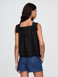 Top senza maniche nero con bordi smerlati e design floreale ricamato, caratterizzato da una vestibilità ampia e un dettaglio sul giromanica posteriore. Abbinato a pantaloncini di jeans.
