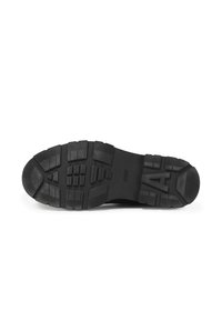 Black rubber outsole with a textured surface, featuring a lug pattern for traction and a raised logo. Flat heel and solid, durable design.