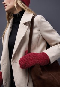 Beige wollen jas met een gestructureerde afwerking, zwarte turtleneck, rode wollen wanten en een bruine suède schoudertas zijn tegen een grijze achtergrond gepresenteerd.