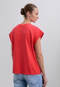 Red cotton t-shirt with short, rolled sleeves, relaxed fit, and a rounded neckline. Visible seam detail at shoulders and hem.