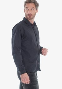 Camisa negra de manga larga con cierre de botones en la parte delantera, cuello y un corte regular; fabricada en un tejido ligero con una textura suave y un brillo sutil.