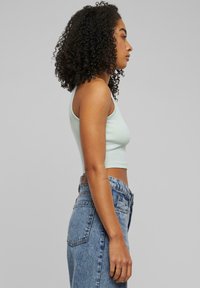 Mätovo zelený cropped tank top vyrobený z rebrovaného materiálu; kombinovaný s vysokými svetlomodrými džínsami v klasickom strihu so zadnými vreckami.
