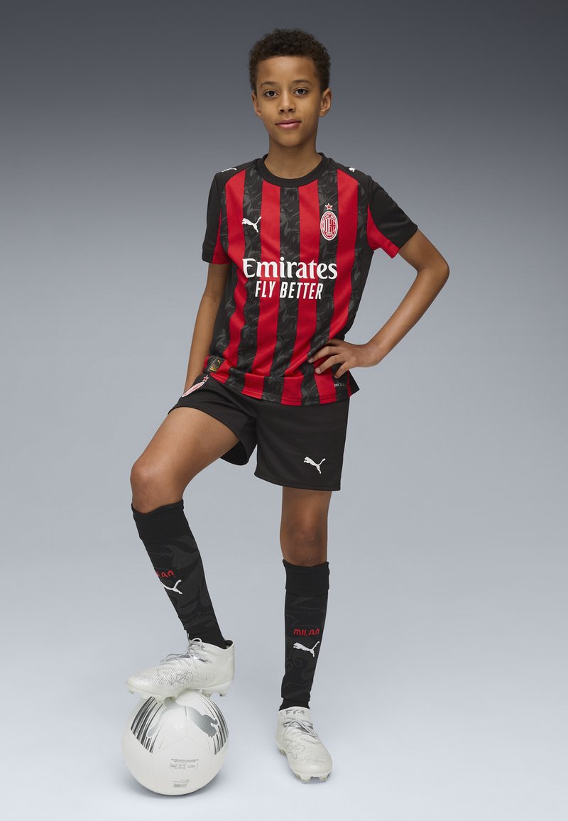 Schwarz-rot gestreiftes Fußballtrikot mit "Emirates"-Logo, schwarze Shorts, schwarze Socken und weiße Fußballschuhe. Auf einem weißen Fußball platziert.