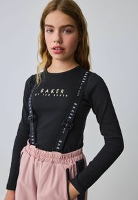 Juodas ilgas rankovėmis palaidinė su auksiniu spaudiniu "BAKER", su reguliuojamomis petnešomis. Šviesiai rožinės kelnės su elastinga juosmeniu ir šoninėmis kišenėmis.