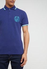 Polo bleu marine avec un col contrastant bleu clair et des accents aux manches, featuring un logo brodé sur la poitrine.
