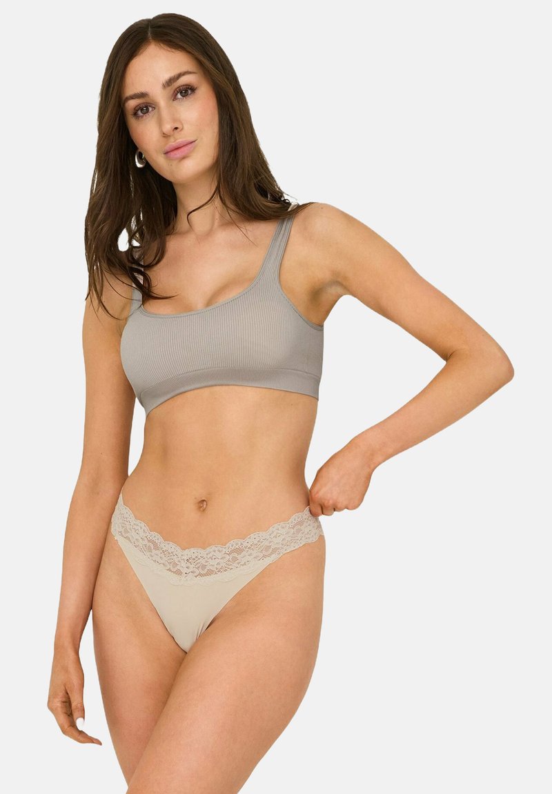 Bralette de canalé gris claro combinado con un tanga nude que presenta una cinturilla de encaje floral. La tela parece suave y elástica.