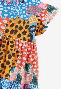 Färggklat lapptäcksklänning med olika mönster: djurtryck, abstrakta former och blommönster i blått, orange, rosa och grönt.