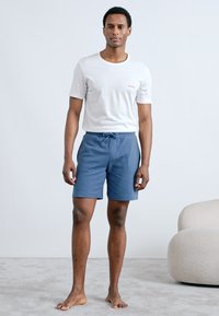 White cotton t-shirt with a small red logo paired with blue checkered shorts featuring an elastic waistband and drawstring.
