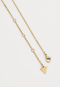 Goldene Kettenhalskette mit einem dreieckigen Anhänger, der mit "GUESS" graviert ist, und einem Karabinerhakenverschluss. Die Kette hat ein Glieddesign.