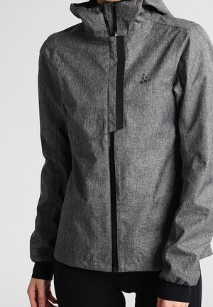 Veste à capuche grise avec fermeture éclair et rabat à l'avant, manches longues, et un petit logo sur le côté gauche de la poitrine, portée par une personne.