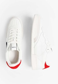 Zapatillas blancas con parte superior de cuero suave, con detalles perforados, acentos en negro y rojo, y una suela de goma texturizada.