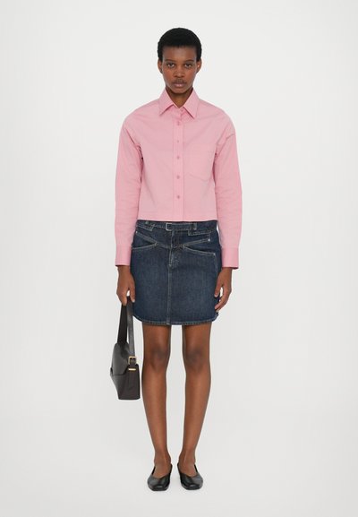 Rosa langermet skjorte med knapper, kort design, parret med en mørk denimskjørt. Svarte flate sko og en brun håndveske fullfører antrekket.