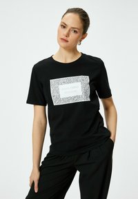 Sort bomulds t-shirt med en hvid rektangulær grafisk tryk med et zebra mønster og teksten "GØR ALLE TING MED KÆRLIGHED." Korte ærmer.