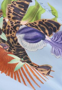 Gros plan d’un tissu avec des motifs détaillés de papillons colorés et de feuilles sur un fond bleu clair, mettant en valeur des textures et des motifs complexes.