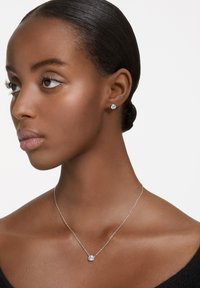 Sølv halskæde med en klar rund vedhæng; matchende ørestikker; glat hudstruktur; sort top; neutral baggrund.