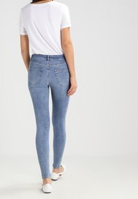 Höga, ljusblå skinny jeans med en slät yta och bakfickor, kombinerat med en åtsittande vit t-shirt och platta vita skor.