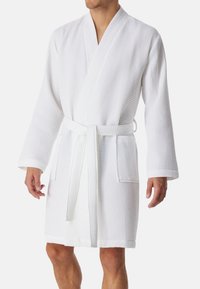 Accappatoio bianco a trama waffle con cintura, maniche lunghe e due tasche frontali. Tessuto leggero e traspirante.