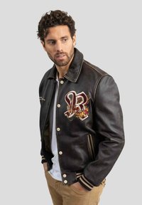 Veste bomber en cuir noir avec un logo brodé rouge et or et un motif de dragon, quincaillerie en argent et accents côtelés aux poignets.
