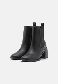 Bottines noires en cuir lisse avec des panneaux latéraux élastiques, bout pointu et talon empilé. Comprend des languettes pour un enfilage facile.