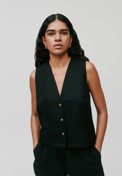 Zwarte mouwloze vest met een V-hals en vijf knopen aan de voorkant. De stof heeft een gladde textuur met een rafelige zoom. Minimalistisch ontwerp.