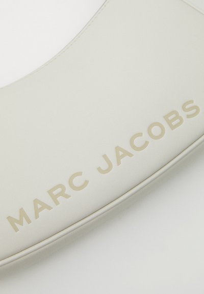 Balta ādas soma ar iepresētu "MARC JACOBS" gaiši bežā krāsā, ar gludu tekstūru un izliekta formu.