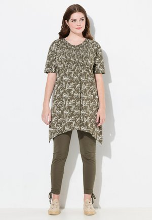 Tunique vert olive avec imprimé floral blanc, avec des manches courtes et un corsage élastiqué ; assortie à des leggings vert olive et des chaussures beiges.