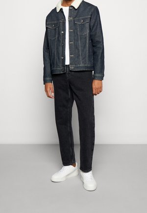 Jeansjakke med hvid shearlingkrave, mørk denimstof, to brystlommer, parret med sorte jeans og hvide sneakers.
