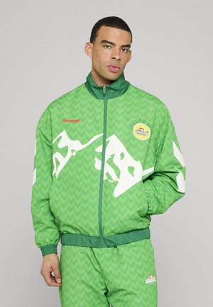 Green tracksuit made of lightweight material, featuring chevron patterns, white accents, and a zippered jacket with a logo and red text.