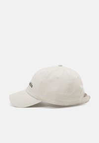 Lys beige baseball cap laget av stoff, med buet skjerm, justerbar reim og brodert merkevarelogo på forsiden.