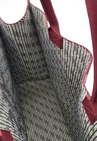 Interno di una borsa a tracolla con un motivo intrecciato in bianco e nero con accenti bordeaux. Il materiale sembra robusto e strutturato con manici in tessuto.