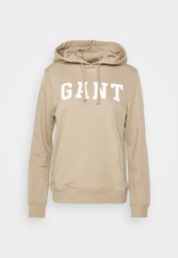 Beige mikina s kapucí a bílým nápisem "GANT", přední kapsou a šňůrkami na stažení. Vyrobena z měkké látky, má dlouhé rukávy a žebrované manžety.