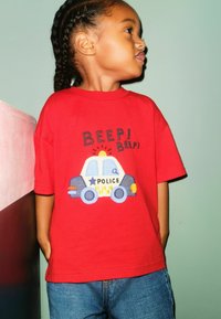 Red cotton t-shirt featuring an embroidered police car design with "BEEP! BEEP!" text. Paired with blue denim jeans.