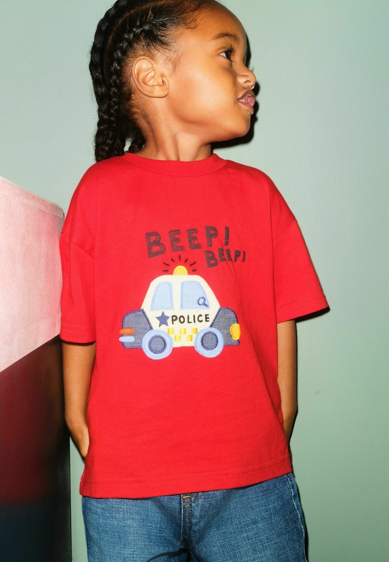 Red cotton t-shirt featuring an embroidered police car design with "BEEP! BEEP!" text. Paired with blue denim jeans.