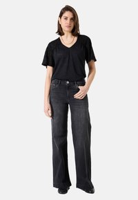 Schwarzes kurzärmliges Oberteil mit strukturierten Spitzeakzenten, kombiniert mit hoch taillierten, weit geschnittenen dunklen Jeans. Einfaches, klares Design ohne Verzierungen.