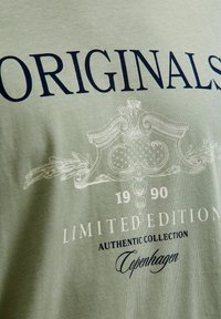 Grøn bomulds T-shirt med marineblå tekst "ORIGINALS" og indviklede hvide grafiske elementer, med "LIMITED EDITION," "1990," og "København."