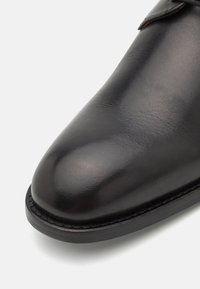 Černá kožená bota s kulatou špičkou, hladkým povrchem a detailním prošíváním podél podešve. Klasický design s lesklým vzhledem.