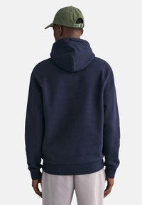 Granatowy hoodie z kapturem, ściągaczami u rękawów i na dole. Noszony z jasnymi spodniami i zieloną czapką. Miękka, fakturowana tkanina.