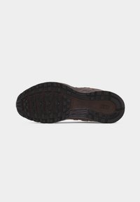 Μαύρη λαστιχένια σόλα παπουτσιού Nike με υφή πέλματος και λογότυπο Nike κοντά στη φτέρνα, εμφανιζόμενη σε απλό φωτεινό φόντο.