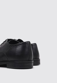 Zapatos de vestir de cuero negro con un acabado suave, que cuentan con cordones, perforaciones decorativas y una suela de goma baja y contrastante.