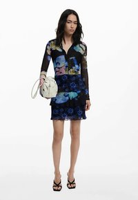 Vestito con motivo floreale, corpetto in rete nera, gonna a balze e dettagli blu. Abbinato a una borsa bianca e tacchi neri con cinturini.