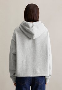 Grijze hoodie met een losse pasvorm, ribgebreide mouwen en zoom, gemaakt van een zachte katoenmix. Gezien vanuit de achterkant tegen een neutrale achtergrond.
