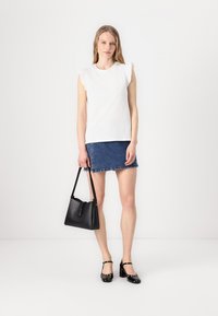 Top alb cu mânecă scurtă și umeri volan, asortat cu o fustă din denim. Geantă neagră cu mânere și pantofi din patent negri. Design minimalist.