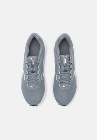 Baskets de sport grises avec tige en mesh, lacets plats et semelle blanche. Caractérisées par un logo sur la languette et le côté, conçues pour le confort et le soutien.