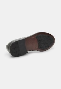Suola di scarpa in pelle con superficie nera liscia, dettagli in pelle marrone, motivo di battistrada testurizzato per una migliore aderenza e forma arrotondata.