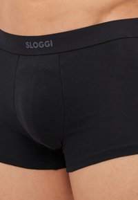 Čierne boxerkové slipy vyrobené z hladkej tkaniny s úzkym elastickým pásom, na ktorom je logo "SLOGGI". Ploché švy zvyšujú komfort.