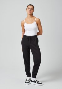 Zwarte sweatpants met een trekkoord in de taille, een witte tanktop en zwart-witte sportieve sneakers. Glad materiaal met elastische boorden.