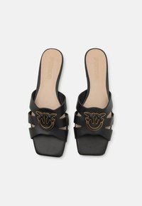 Crne slide japanke s glatkom teksturom, s tri široke trake i zlatnim smiley logom. Bež uložak s "PINKO" brendiranjem.